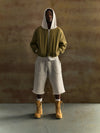 Person wearing a green hoodie, gray pants, and yellow boots against a brown background