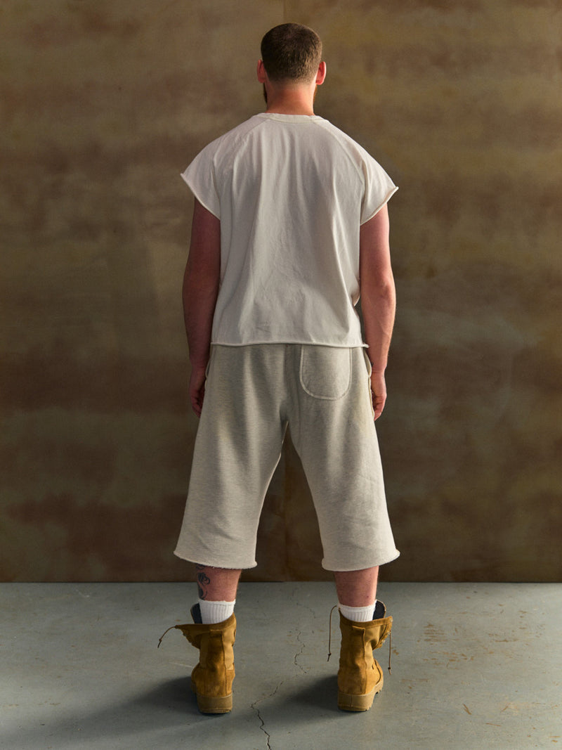 Person wearing a white t-shirt and beige shorts with brown boots against a textured wall.