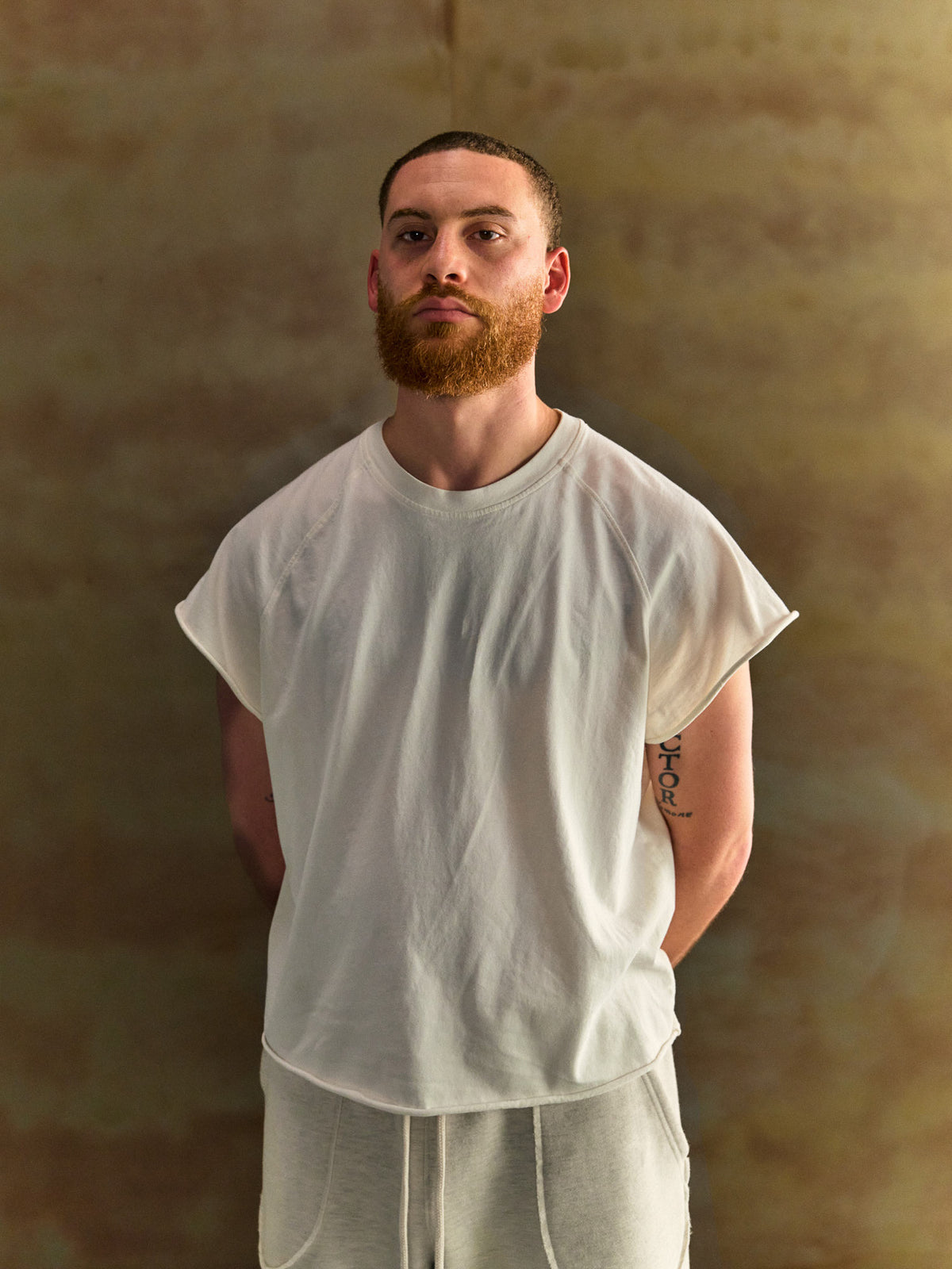 Man wearing a plain white t-shirt and pants against a textured brown background